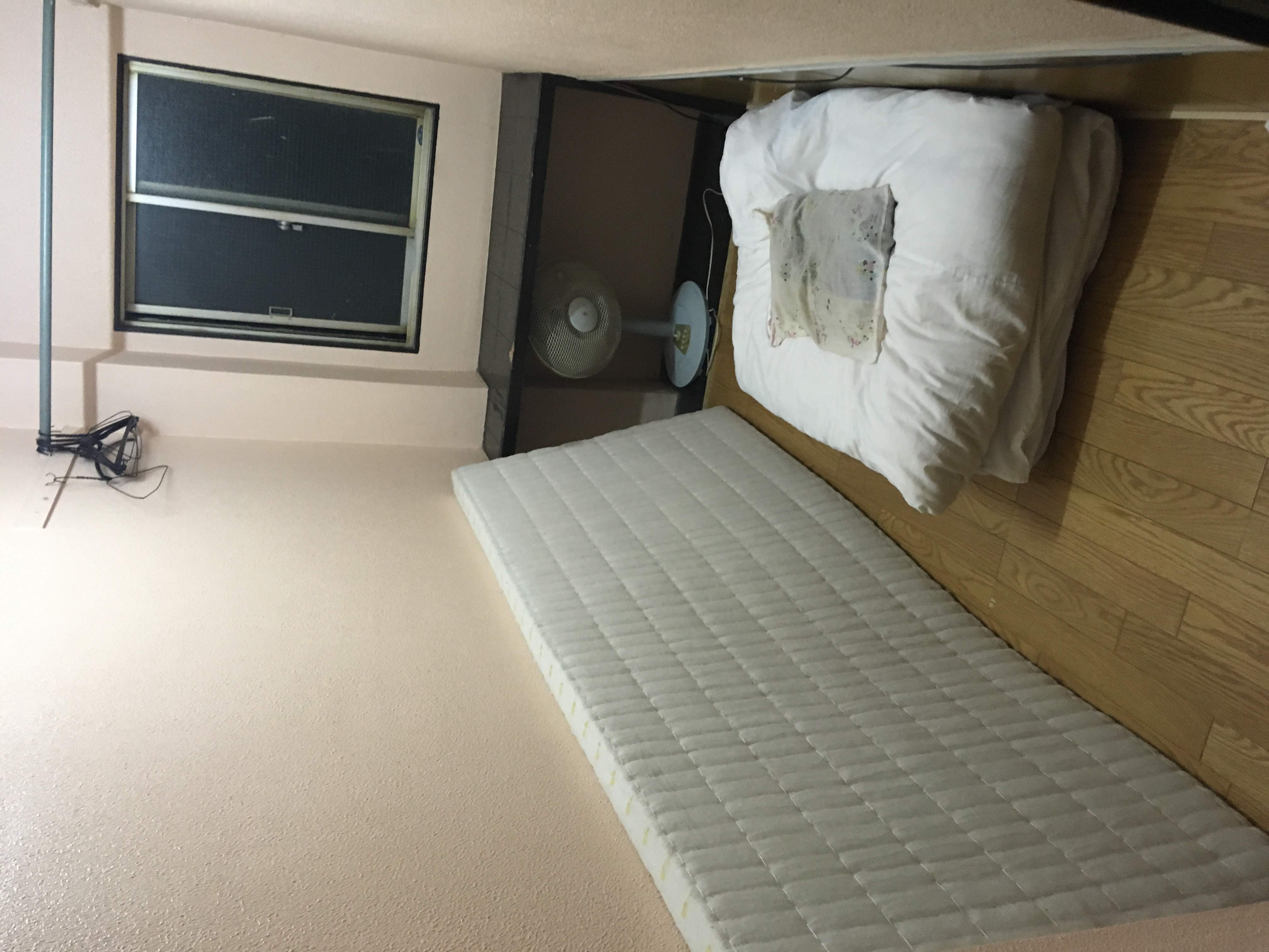 Small hotel room with bed, desk, and open circulation path in a narrow footprint.